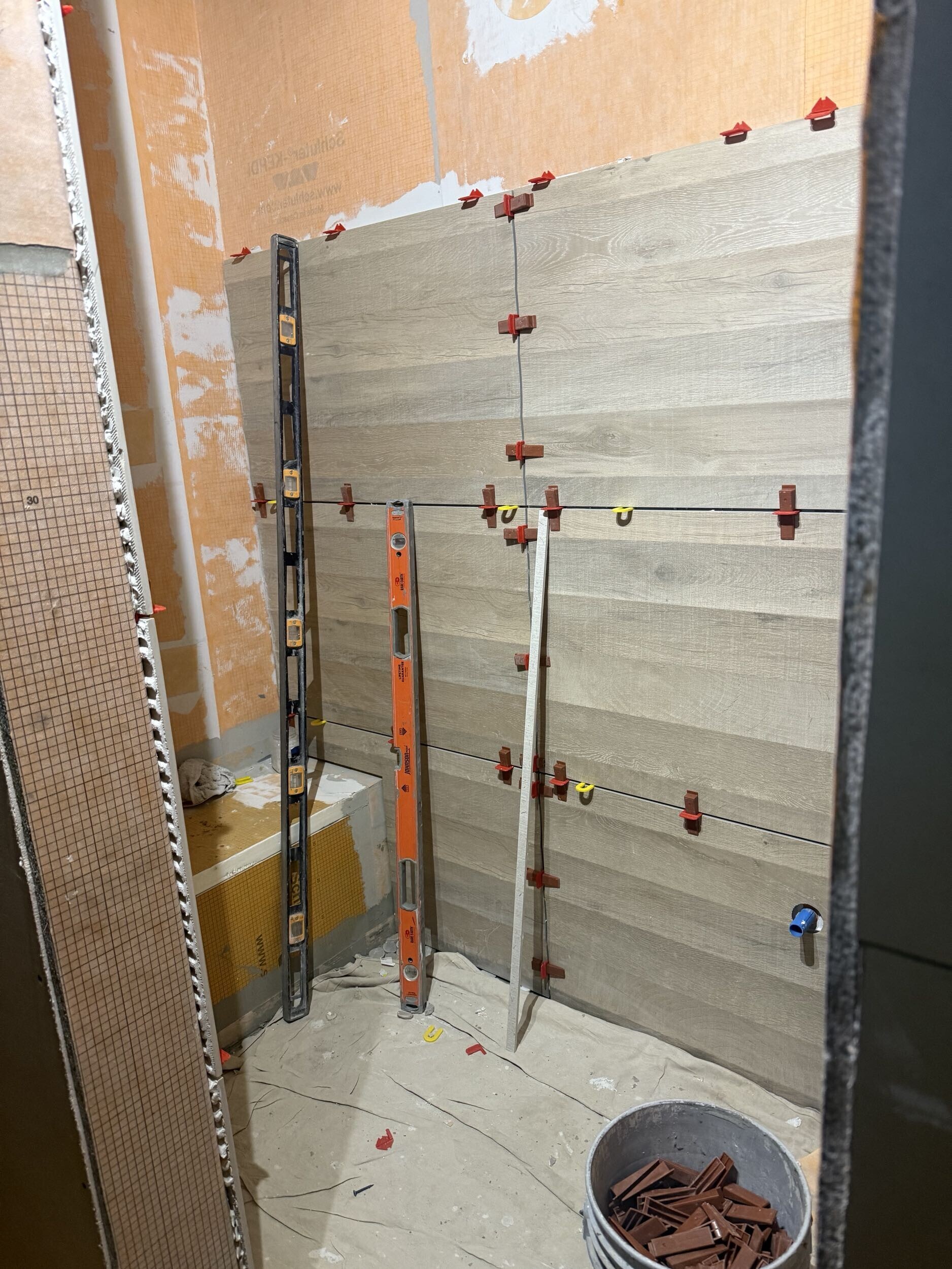 Bathroom remodel in progress with large-format shower wall tile installation, using leveling clips and levels to ensure precise alignment and minimal grout lines.